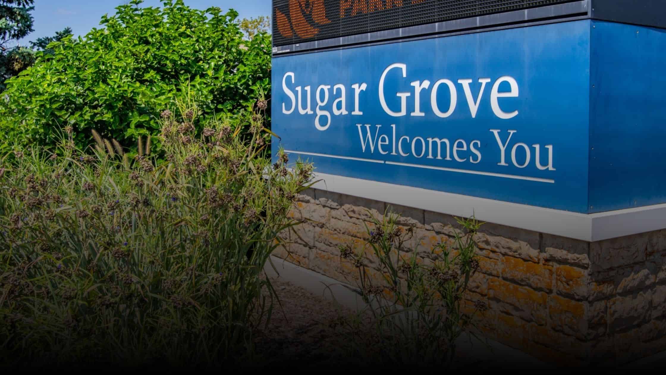 Signboard in Sugar Grove, Illinois, with the message "Sugar Grove Welcomes You," surrounded by greenery